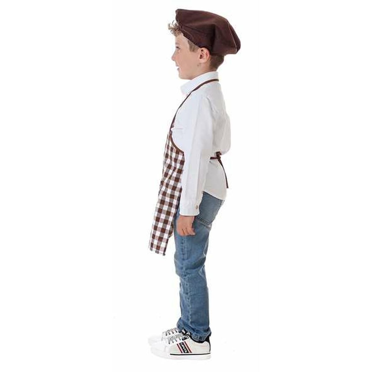 En pojke sedd från sidan bär en brun och vitrutig kockförkläde och en mörkbrun basker över en vit skjorta och jeans.