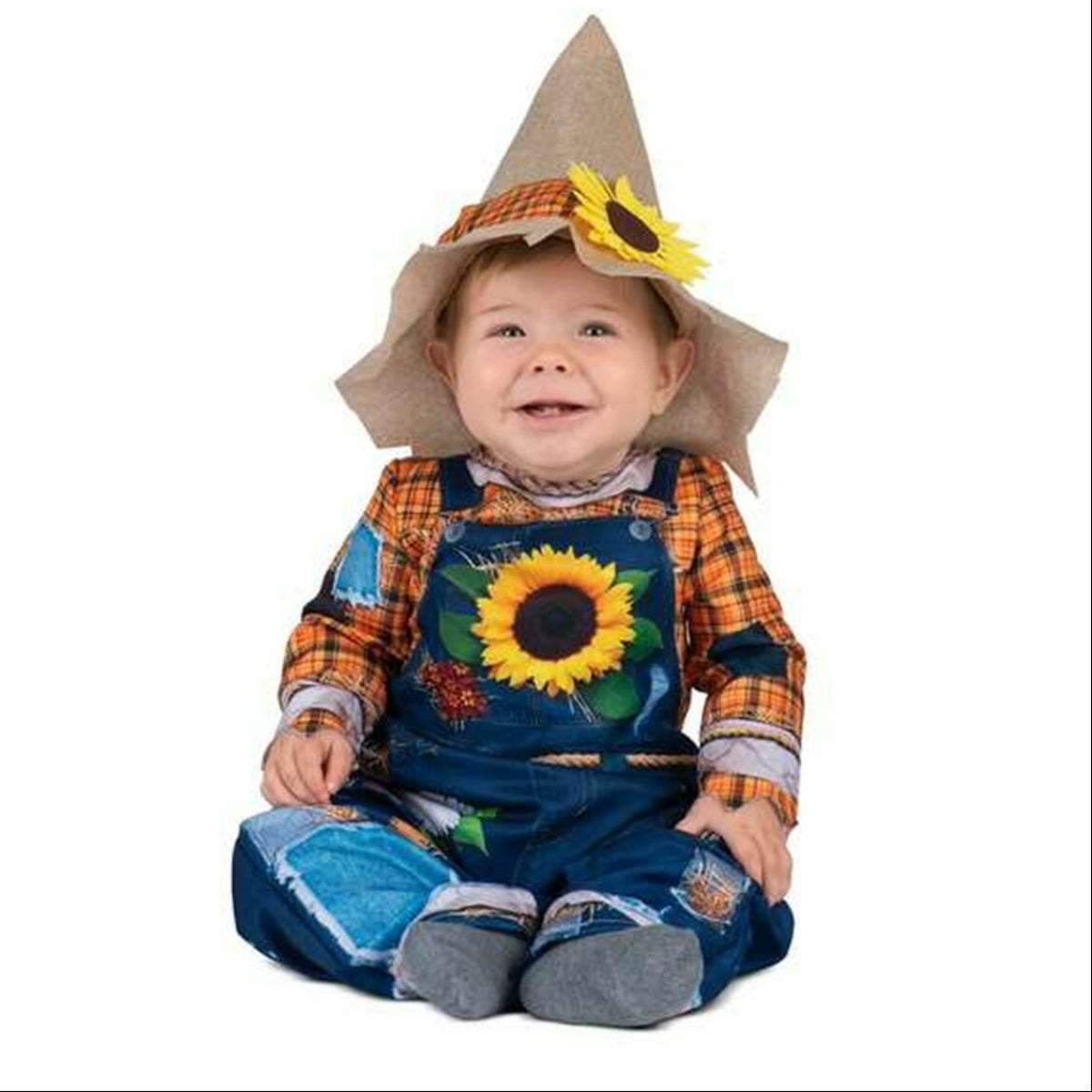 En glad bebis sitter på golvet i en charmig och komplett fågelskrämma-dräkt med hängselbyxor, hatt och en stor solros.