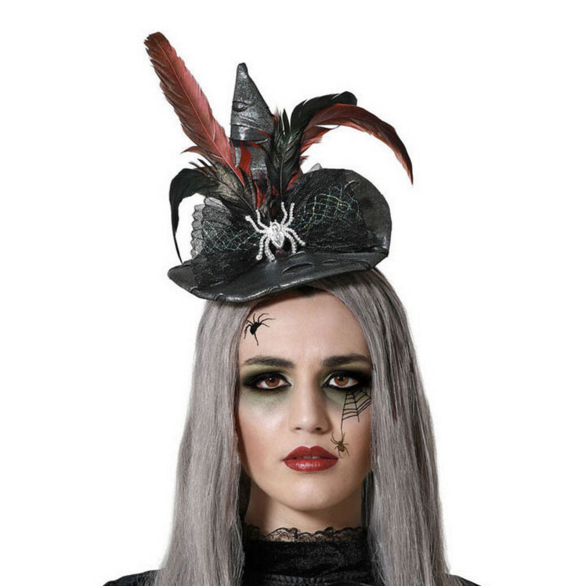 Närbild på en kvinna med grått hår och dramatisk sminkning som bär ett diadem med en gotisk mini-häxhatt, dekorerad med fjädrar och en glittrande spindel.