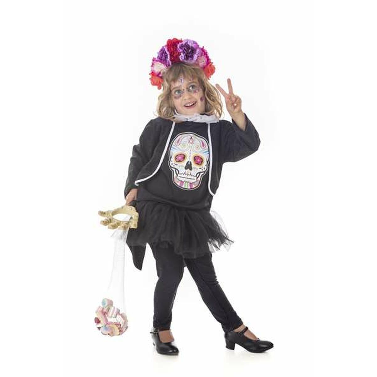 Ett barn i en svart Catrina maskeraddräkt med en stor färgglad dödskalle på tröjan, en blommkrans på huvudet och som håller i en liten nätsäck med godis.