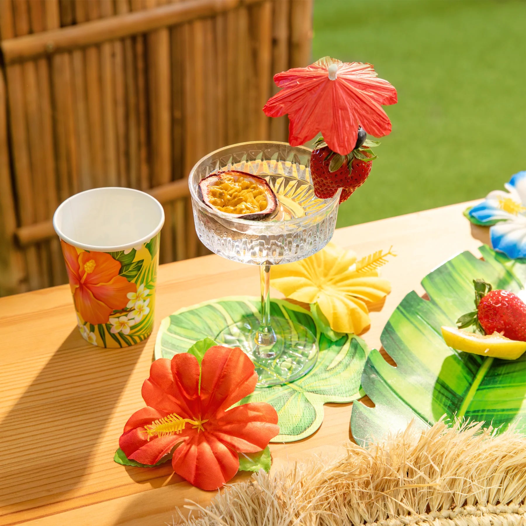 En tropisk dukning med drinkglas, frukt, parasoll och färgglada Hawaii tygblommor som dekoration på bordet.