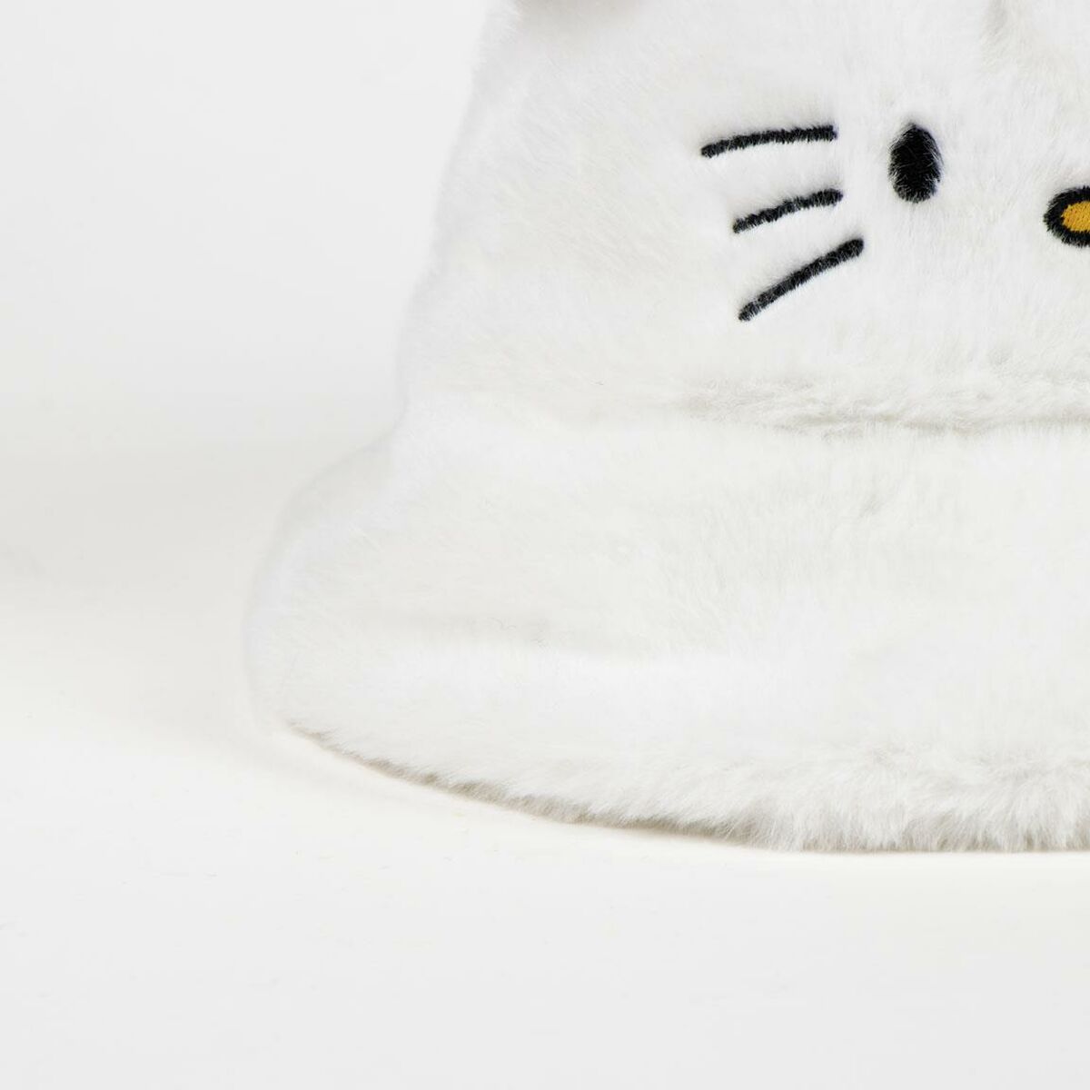  En närbild på den vita, fluffiga hatten som visar detaljerna i det broderade morrhåret.