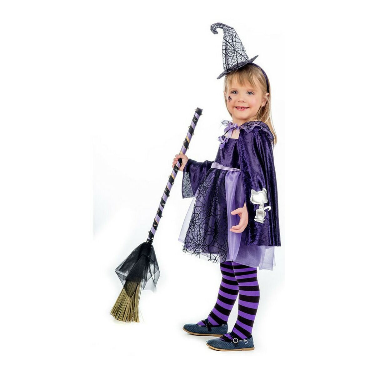 En glad flicka i en lila häxdräkt med stjärnor och spindelvävsmönster, komplett med cape, hatt och randiga strumpbyxor.