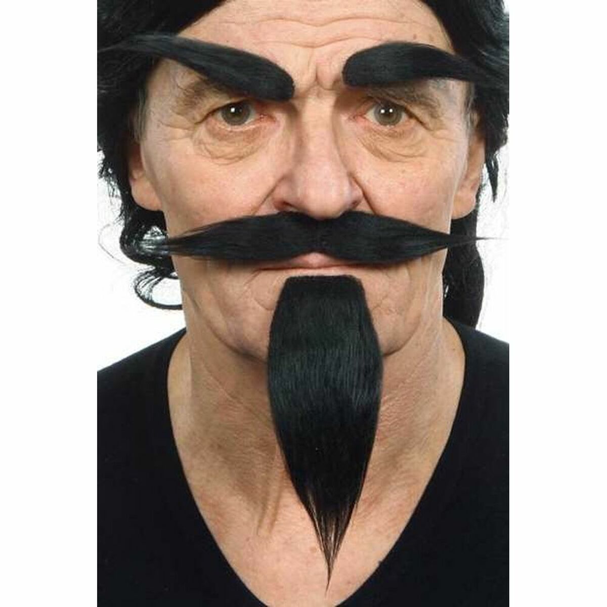 En man med en ondskefull, intensiv blick bär ett komplett set med svart lösskägg, mustasch och tjocka, spetsiga ögonbryn, fotograferad i en studio.