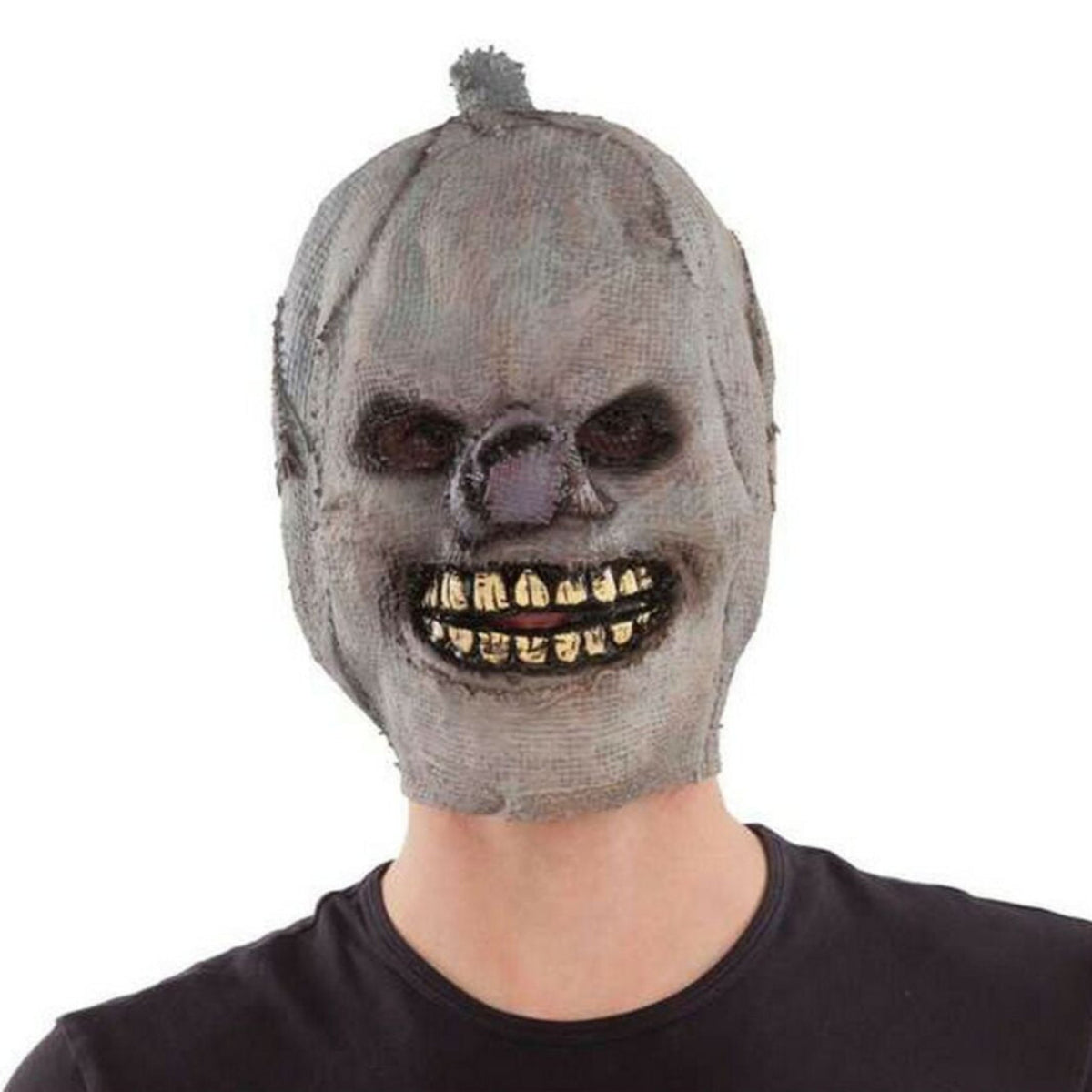 En person bär en läskig, heltäckande halloweenmask som ser ut att vara gjord av grå säckväv, med svarta ögonhålor och ett brett, ondskefullt leende med gula tänder.